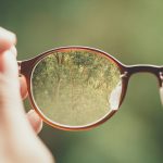 person holding brown eyeglasses with green trees background